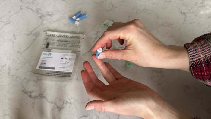 A woman using the lancet included in the LetsGetChecked Cholesterol test kit to prick her finger for the blood sample collection.